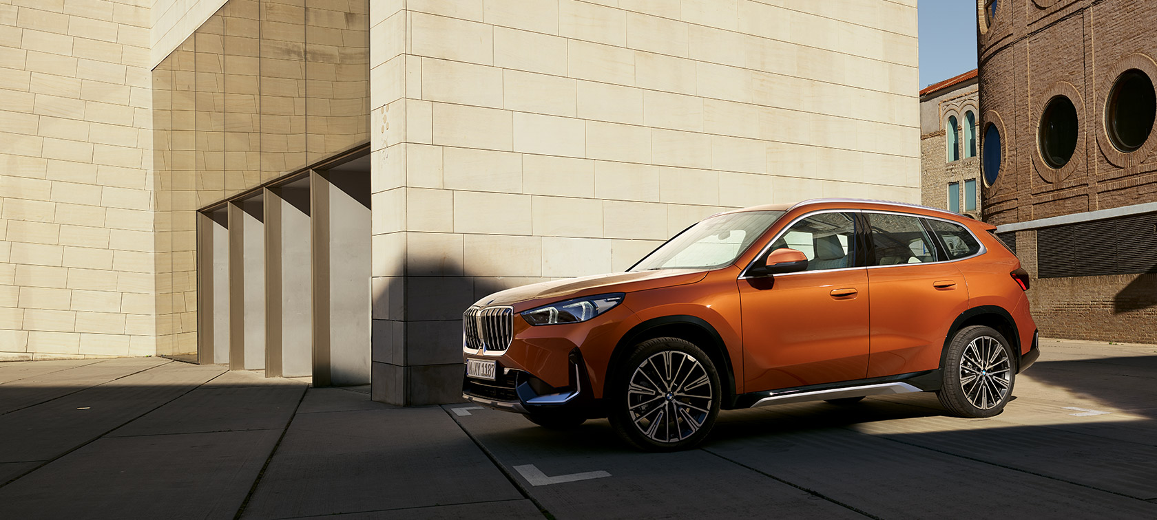 BMW U11 X1 xLine Utah orange metallic three quarter front view still in front of building